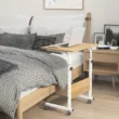 Compact oak wood bed table with a white metal frame, designed for working or eating in bed, with a laptop placed on top.