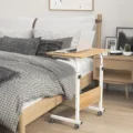 Compact oak wood bed table with a white metal frame, designed for working or eating in bed, with a laptop placed on top.