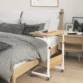 Compact oak wood bed table with a white metal frame, designed for working or eating in bed, with a laptop placed on top.