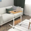 Oak wood bed table with a white metal frame, adjustable height, and rolling wheels, holding a laptop, ideal for use on a couch or bed.