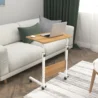 Oak wood bed table with a white metal frame, adjustable height, and rolling wheels, holding a laptop, ideal for use on a couch or bed.