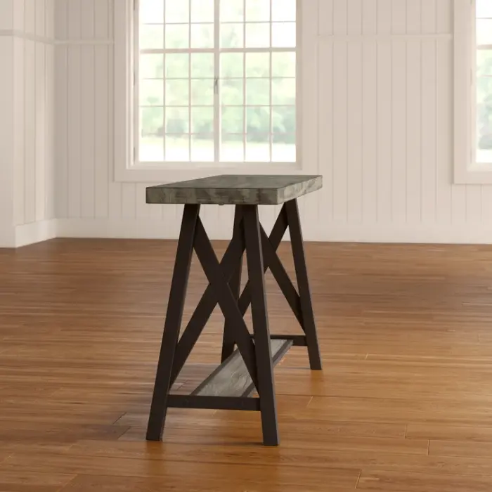 Side view of the ForgeLine Console Table in Gray, showcasing its rustic wood tabletop and black metal trestle-style legs, set on a warm wooden floor.