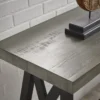 Close-up of the ForgeLine Console Table in Gray, highlighting its distressed wood grain tabletop and sturdy black metal legs against a white brick wall.