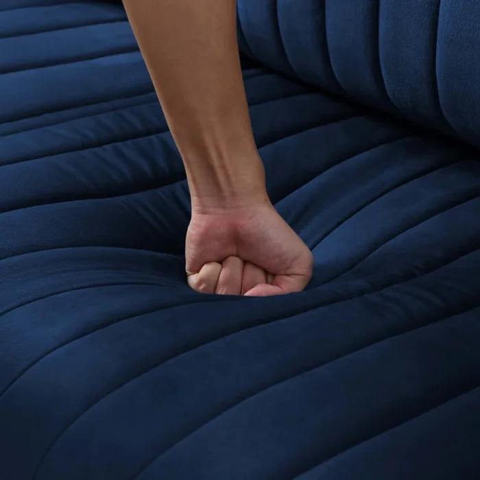 Hand pressing into the plush, tufted seat cushion of the Aurello Velvet Chair in navy blue velvet.