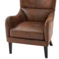 Close-up of Crown upholstered wingback chair seat with curved armrests, rustic brown faux leather, and black wooden legs