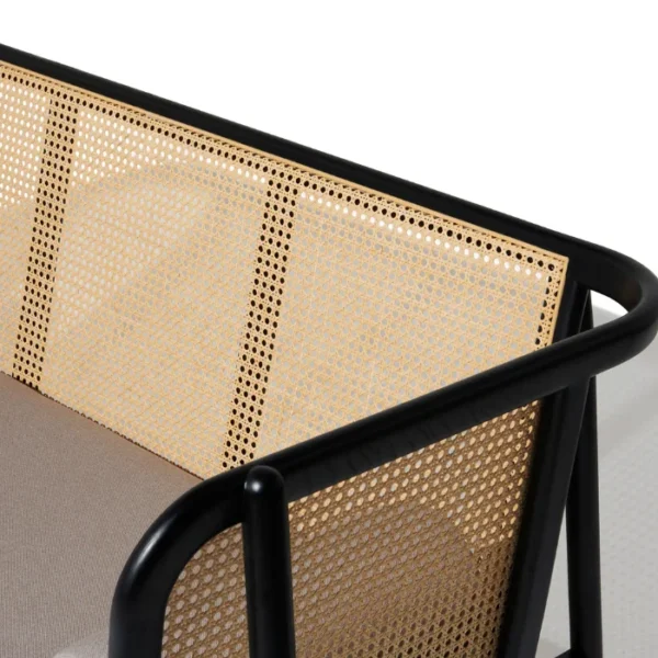Close-up of black cane sofa with handwoven rattan backrest and beige cushion, featuring a solid wood frame Close-up of black cane sofa with handwoven rattan backrest and beige cushion, featuring a solid wood frame