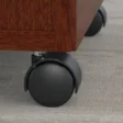 Close-up of black caster wheel beneath mahogany mobile pedestal on office carpet.