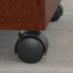 Close-up of black caster wheel beneath mahogany mobile pedestal on office carpet.