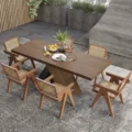 Cane Dining Set – modern wooden dining table with sculptural crossed base and six cane-back armchairs in a warm wood finish, styled in a contemporary indoor/outdoor setting.