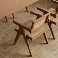 Close-up of a cane-weave armchair with solid wooden frame beside the dining table on herringbone flooring.