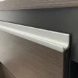 Detail of sleek aluminum edge pull on wood cabinet panel with matte black accent.