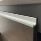 Detail of sleek aluminum edge pull on wood cabinet panel with matte black accent.