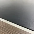 Close-up of textured black leather desk inlay bordered by metallic trim and walnut veneer.
