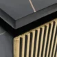 Close-up of black nightstand corner showing layered top and gold fluted drawer detail, textured.