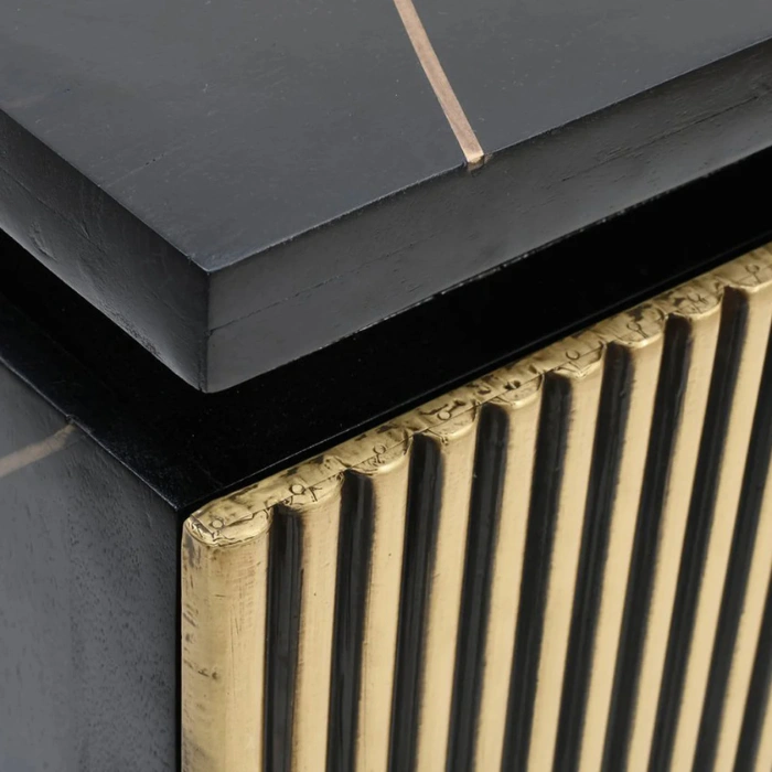 Close-up of black nightstand corner showing layered top and gold fluted drawer detail, textured.