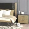 Black-and-gold nightstand beside upholstered bed, fluted drawers and handles in a contemporary bedroom.