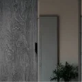 Close-up of charcoal wood sliding door with recessed pull beside a mirrored panel—modern wardrobe detail