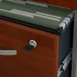 Close-up of lockable file drawer with hanging folders in cherry finish and metal slides.