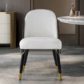 Front view of white leatherette dining chair with gold-tipped black legs in a modern dining room.