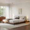 Modern bedroom with a low-profile platform bed featuring an upholstered headboard and walnut frame, flanked by floating nightstands near a large sunlit window.