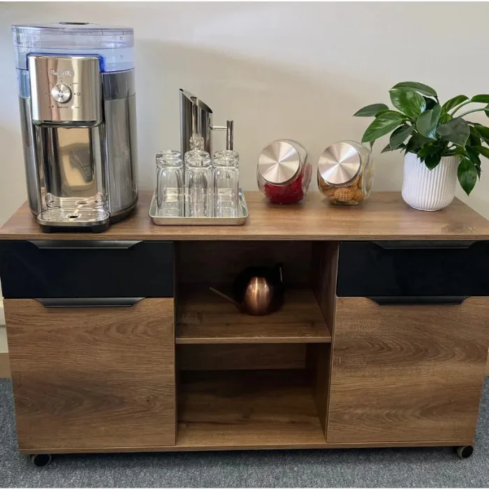 Beverage station cabinet with glass tray, jars, plant, and center open shelf; side doors and drawers on locking casters.