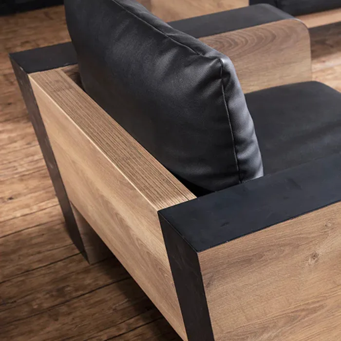 Close-up of armrest showing black cushion, matte black trim, and natural wood grain panel.