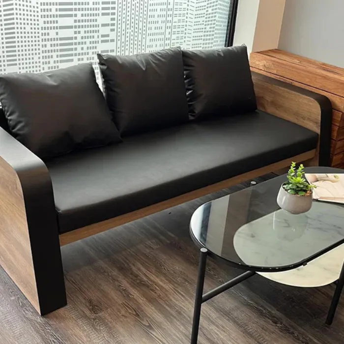 Oak Sofa three-seater in office setting with black cushions and matte upholstery beside a glass coffee table.