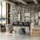 Industrial-style office lounge scene with wood-grain sided 3-seater sofa and black cushions, paired with geometric coffee table and shelving in the background.