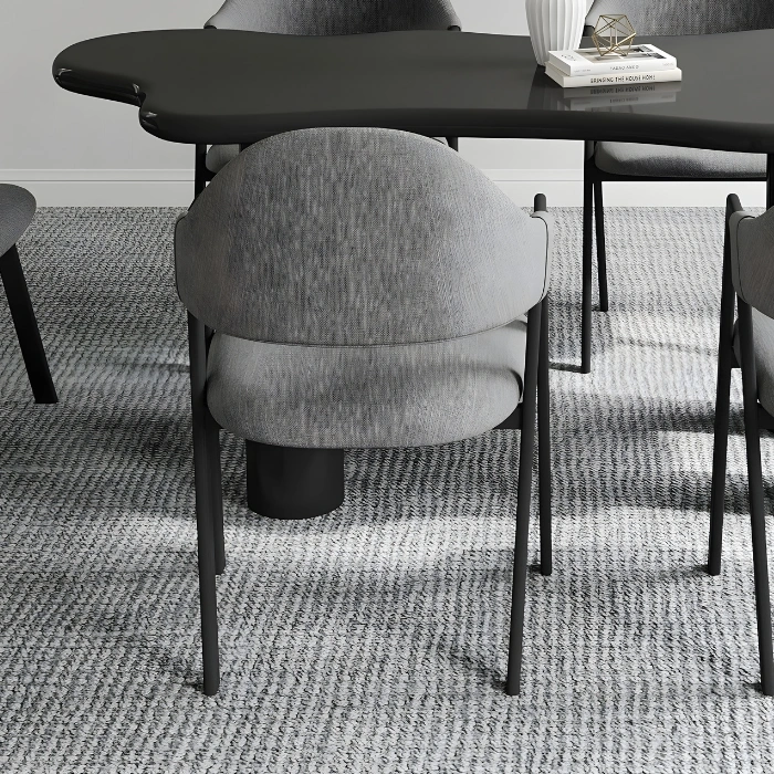 Rear view of a rounded grey dining chair tucked to a sculpted black table on a textured rug.