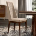 Beige upholstered high-back dining chair beside a veneered table in a modern room.