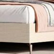 Close-up of ribbed cream side panel, mattress corner, and tapered metal leg with throw blanket