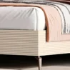 Close-up of ribbed cream side panel, mattress corner, and tapered metal leg with throw blanket