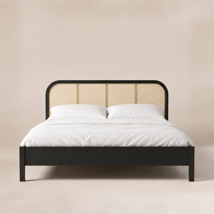 Black cane bed viewed from the front, with a rounded headboard, white duvet and open space beneath the frame.