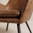 Close-up of Varden Lounge Armchair brown leatherette upholstery, piping and black metal leg