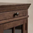 Close-up of Brown Wash wood grain, moulded top, and antique-style metal drawer knob.