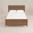 Front view of Aldren wooden platform bed with warm brown finish, tall panel headboard, framed footboard, and turned legs.
