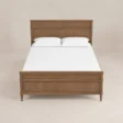Front view of Aldren wooden platform bed with warm brown finish, tall panel headboard, framed footboard, and turned legs.