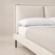Close-up of Nolven Softline Upholstered Bed in warm ivory fabric showing the padded headboard and slim metal legs.