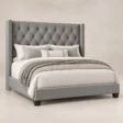 Angled view of Bellmere Wingback Bed in grey upholstery with diamond-tufted headboard and nailhead trim.