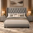 Bellmere Wingback Bed in grey upholstery with diamond-tufted headboard, nailhead trim, and matching bedside tables in a styled bedroom.