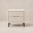 Nolven Softline matching two-drawer bedside table in warm ivory upholstery with slim black metal legs.