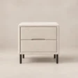 Nolven Softline matching two-drawer bedside table in warm ivory upholstery with slim black metal legs.