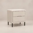 Angled view of Nolven Softline matching two-drawer bedside table in warm ivory upholstery with slim black metal legs.