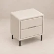 Angled top view of Nolven Softline matching two-drawer bedside table in warm ivory upholstery with slim black metal legs.