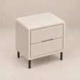 Angled top view of Nolven Softline matching two-drawer bedside table in warm ivory upholstery with slim black metal legs.