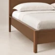 Close-up of Kelden Linea Bed in Walnut Brown finish showing the wooden frame, side rail, and slim tapered leg.